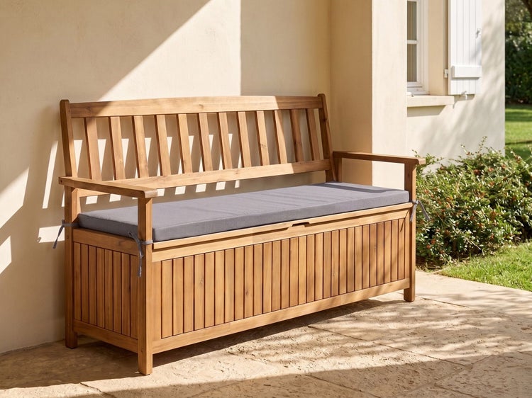 Gartenbank aus Holz mit integrierter Auflagenbox und grauem Sitzkissen, stehend auf einer Terrasse an einer Hauswand.