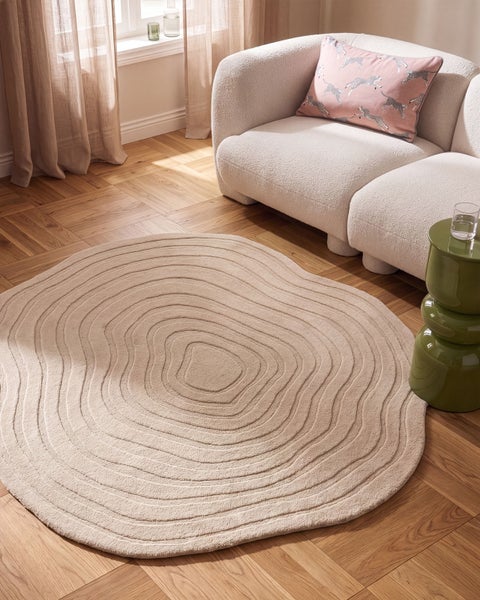 Runder Wohnzimmerteppich mit strukturiertem Wellenmuster auf einem Holzboden vor einem Sofa in einer hellen Wohnumgebung.