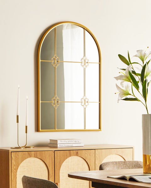 Dekorativer Spiegel mit goldenem Rahmen über einem Sideboard mit Kerzenständer und Blumenvase.