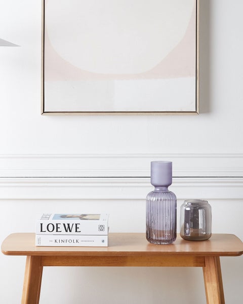 Dekoratives Arrangement mit zwei Glasvasen und Büchern auf einem Holztisch unter einem gerahmten Bild an einer weißen Wand.