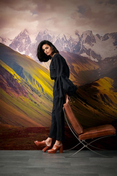 Frau posiert vor einer Fototapete mit Berglandschaft und lehnt an einem Sessel.