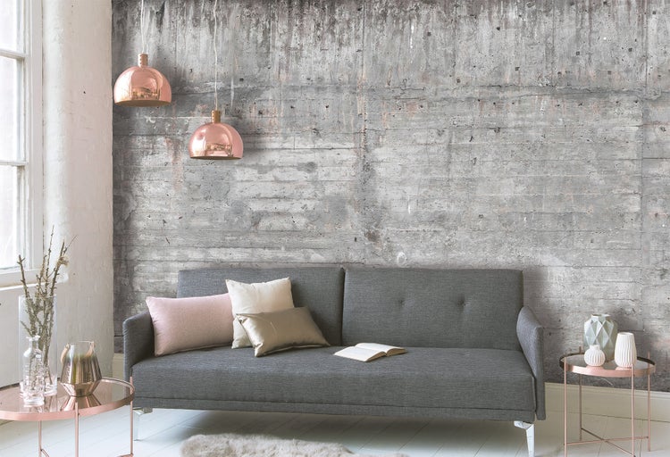 Fototapete in Betonoptik mit horizontalen Linien in einem modern eingerichteten Wohnzimmer mit grauem Sofa und kupferfarbenen Hängelampen.