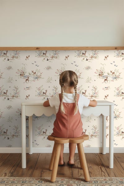 Ein Kinderzimmer mit einer Tapete mit Reh-, Blumen- und Vogelmotiven, einem weißen Schreibtisch und einem Holzhocker