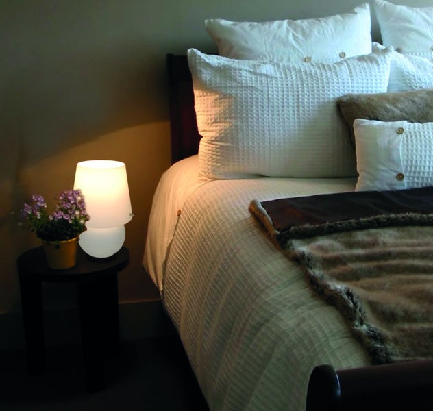 Schlafzimmer mit Nachttischlampe und Dekoration auf dem Nachttisch neben einem Bett