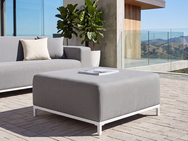 Moderner Loungehocker für den Außenbereich mit quadratischem Design, Textilbezug und stabilem Gestell auf einer Terrasse.