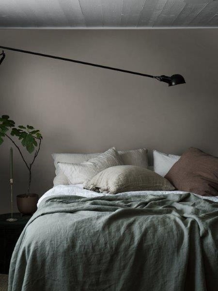 Schlafzimmer mit Bett, Kissen, Tagesdecke, Pflanze und einer Wandlampe.