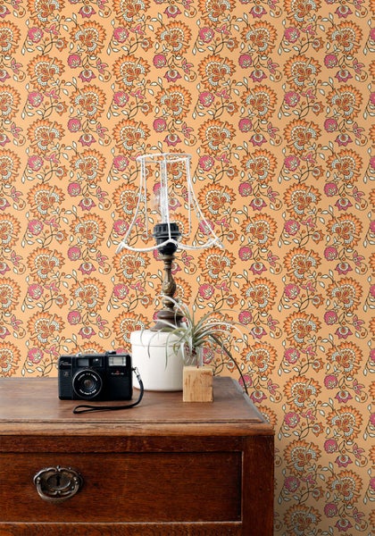 Gemustertes Zimmer mit Tisch, Lampe und Kamera vor einer floralen Tapete