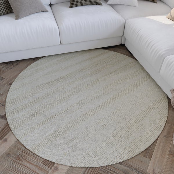 Runder, strukturierter Teppich auf einem Holzfußboden vor einem Sofa in einem hellen Wohnzimmer.