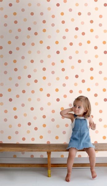 Ein Mädchen sitzt vor einer Wand mit Punktmuster auf einer Holzbank.