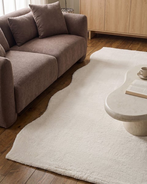 Flauschiger, weißer Teppich in organischer Form auf Holzboden neben einem Sofa und einem Couchtisch aus Marmor.