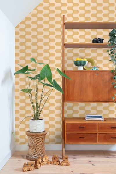 Retro-Tapete mit geometrischem Wellenmuster in Senfgelb, kombiniert mit einem Holzregal und einer Zimmerpflanze im Mid-Century-Stil.