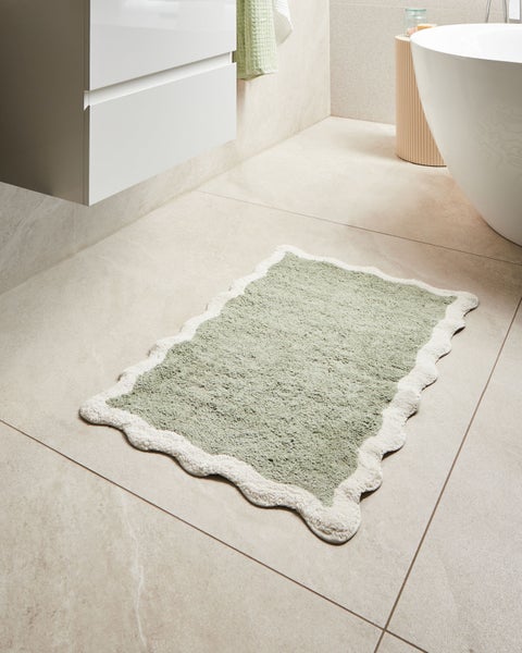 Badezimmer mit Waschbeckenunterschrank, Badewanne und Badteppich mit Muschelkante