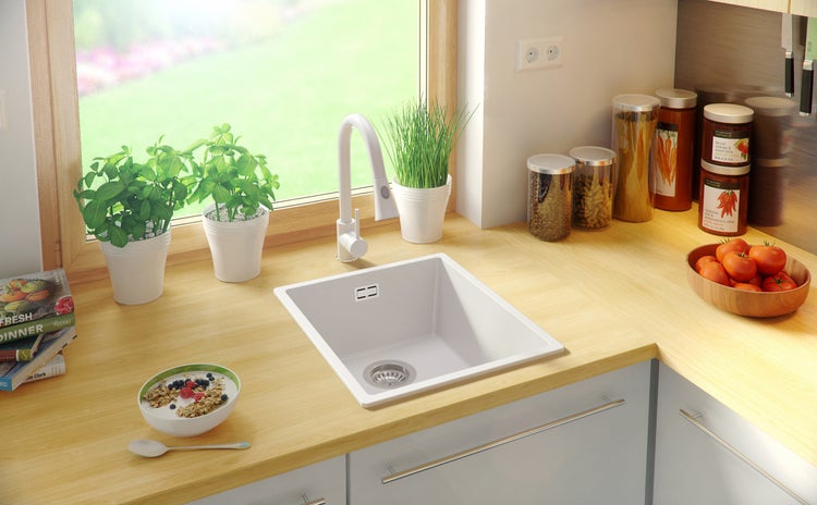 Küchenspüle in einem hellen Küchendesign mit Armatur, Kräutern und Lebensmitteln