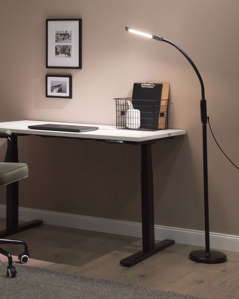 Schreibtisch mit Stehlampe, Laptop und Bürobedarf für einen organisierten Arbeitsplatz