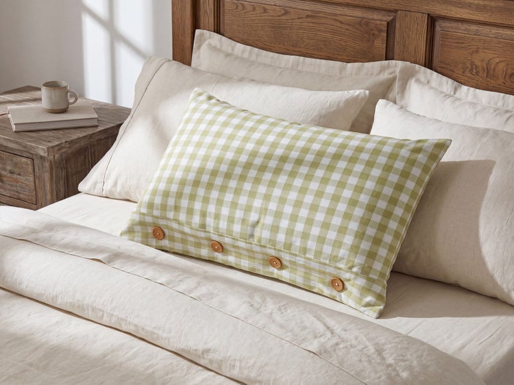 Helles Schlafzimmer mit Holzbett, Leinenbettwäsche und einem karierten Zierkissen mit Holzknöpfen im Vordergrund.