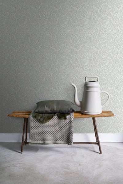 Tapete mit Blattmuster, Gießkanne und Kissen auf einer Bank