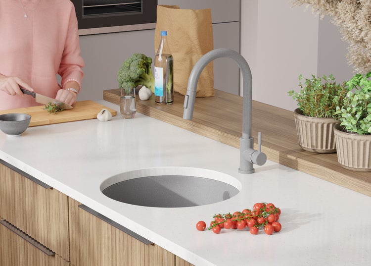 Küchenszene mit Spüle, Armatur, Gemüse, Kräutern und Person beim Kochen