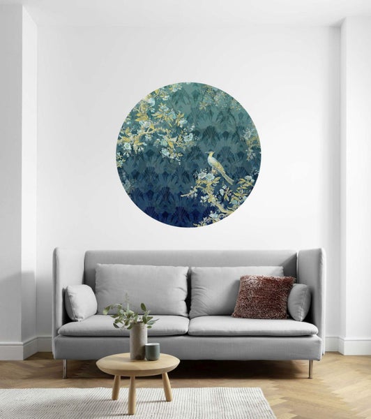 Wohnzimmer mit rundem Wandbild mit Vogel- und Blumenmuster über einem grauen Sofa.
