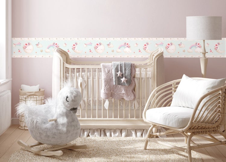 Tapetenbordüre mit Regenbogen, Mond und Sternen in einem hellen Babyzimmer mit Holzgitterbett und Korbsesseln.