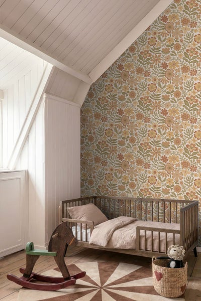 Helles Kinderzimmer unter einer Dachschräge mit floraler Mustertapete, hölzernem Kinderbett, Schaukelpferd aus Holz und einem runden Teppich.