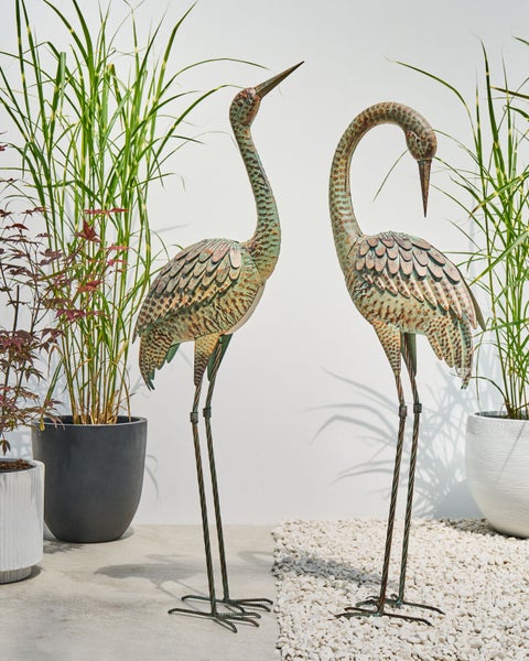 Dekorative Gartenfiguren: Zwei Reiher aus Metall zwischen Gräsern und Pflanzenkübeln