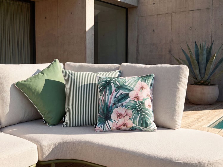 Drei quadratische Dekokissen in einem modernen Gartenbereich auf einem hellen Outdoor Sofa platziert, eines mit floralem Muster.