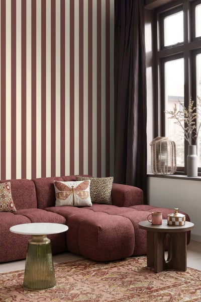 Gestreifte Tapete mit vertikalen Bahnen in Rot und Creme in einem Wohnzimmer mit rotem Sofa und Beistelltischen.