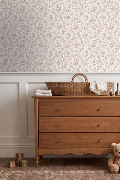Tapete mit floralem Muster in einem hellen Kinderzimmer mit weißer Wandvertäfelung und einer Holzkommode mit Weidenkorb im organisierten Stil.