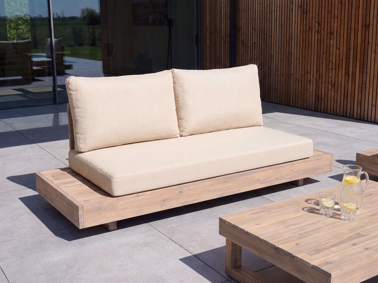 Modernes Gartensofa aus Holz mit hellen Polsterauflagen auf einer Terrasse vor einer modernen Hausfassade mit Holzelementen.