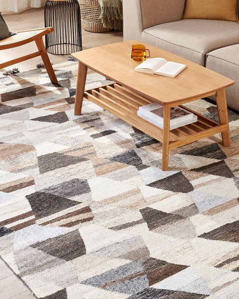 Webteppich mit geometrischem Dreiecksmuster in hellen Naturtönen in einem modern eingerichteten Wohnzimmer mit Couch und Holztisch.