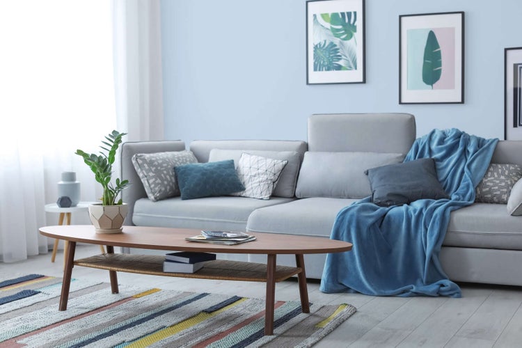 Modernes Wohnzimmer mit grauer Eckcouch, ovalem Couchtisch aus Holz, gestreiftem Teppich und botanischen Wandbildern.