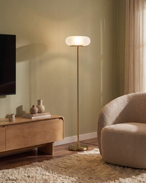 Moderne Stehleuchte mit rundem Glasschirm und schlankem Metallständer neben einem TV-Board in einem gemütlich eingerichteten Wohnzimmer.
