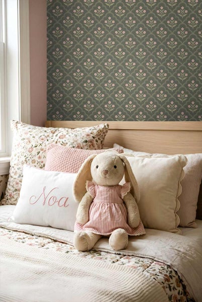 Kinderzimmer mit Mustertapete mit floralen Bögen, Holzbett mit verschiedenen Dekokissen und einem Stoffhasen.