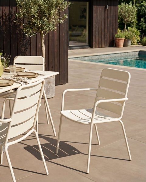 Moderner Gartenstuhl aus Metall auf einer Terrasse neben einem Pool und einem Gartentisch vor einer dunklen Holzfassade.