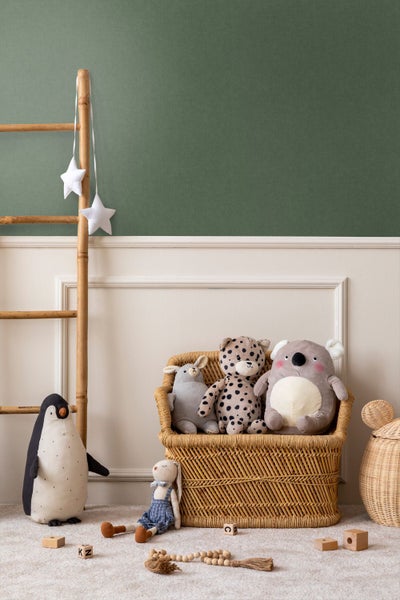 Kinderzimmer mit zweifarbigem Wanddesign in Grün und Beige, dekorativen Wandleisten, einer Holzleiter und einem Korbstuhl mit Stofftieren.