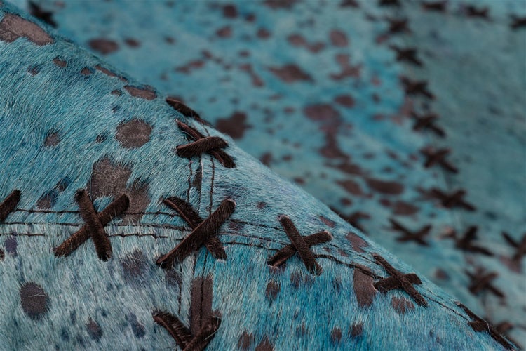 Nahaufnahme eines blau eingefärbten Kuhfellteppichs mit Kreuzstich-Details.