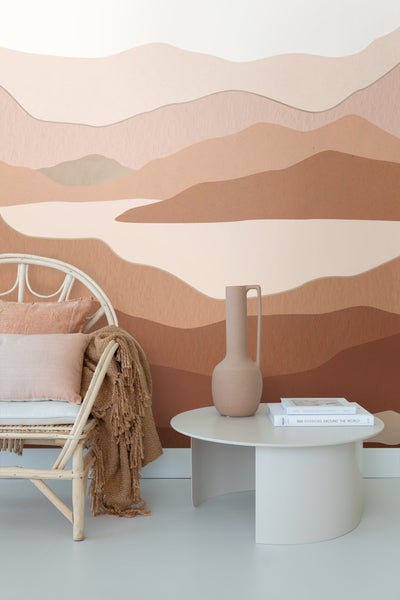 Szene mit Rattan-Sessel, Kissen, Überwurf, Vase, Büchern und Wandbild mit Landschaftsmotiv