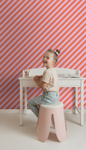 Kind sitzt an einem weißen Schreibtisch mit Stuhl vor einer gestreiften Tapete