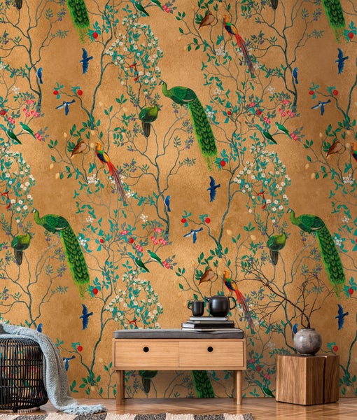 Vliestapete mit Chinoiserie-Muster, Pfauen und Blüten vor goldenem Hintergrund hinter einer modernen Holzkommode in einem hellen Wohnraum.