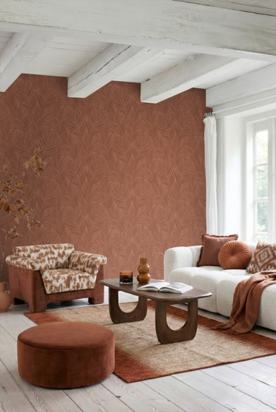 Wohnzimmer mit terracottafarbener Tapete mit Blattmuster, weißem Sofa, braunem Sessel und Holztisch unter weißer Balkendecke.