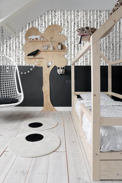 Helles Kinderzimmer mit Holzbett, Baumregal, Schaukelstuhl und runden Teppichen