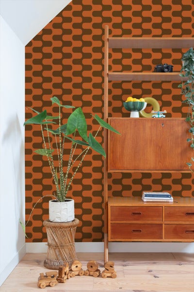 Retro-Tapete mit geometrischem Wellenmuster in Orange und Braun in einem Zimmer mit Holzregal und großer Zimmerpflanze.