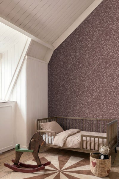 Kinderzimmer mit geblümter Vliestapete an der Dachschräge, einem hölzernen Gitterbett, Schaukelpferd und hellen Holzpaneelen an Decke und Wand.