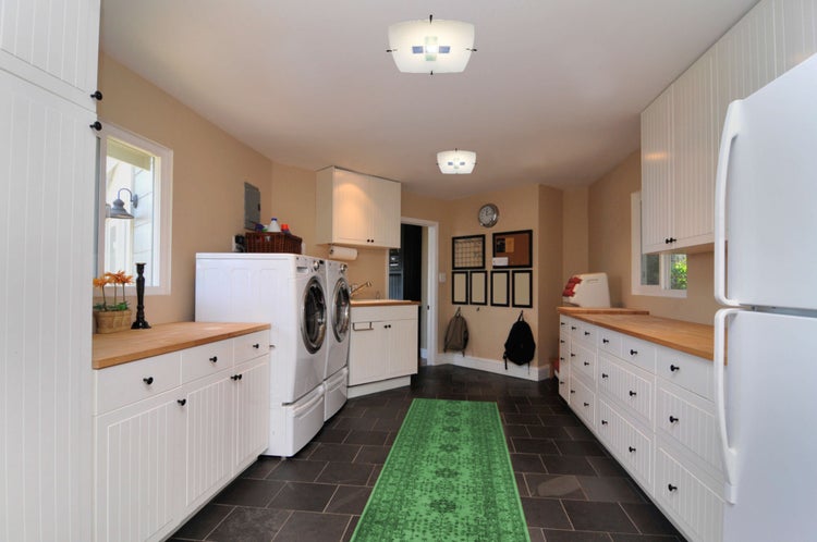 Heller Waschraum mit Waschmaschine, Trockner, weißen Schränken, Holzoberflächen und grüner Matte