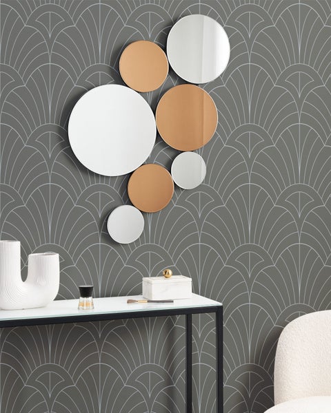 Dekorative Szene mit runden Spiegeln, Konsole, Vase und Sessel vor einer gemusterten Wand