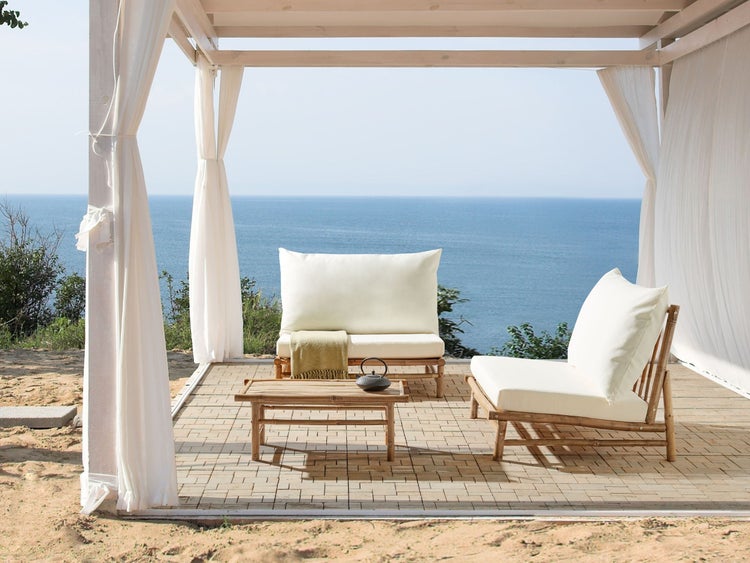 Terrasse mit Bambusmöbeln, darunter Sessel, Bank und Tisch, unter einem Baldachin mit Vorhängen