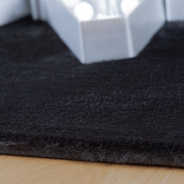 Detail eines weichen, schwarzen Hochflor-Teppichs auf hellem Holzboden.