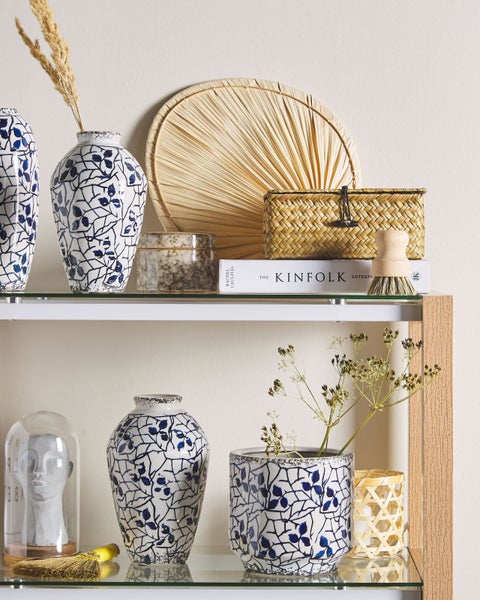 Dekorative Gegenstände auf einem Regal, darunter Vasen, eine Dose, ein Korb, eine Bürste, ein Fächer und eine Glaskuppel