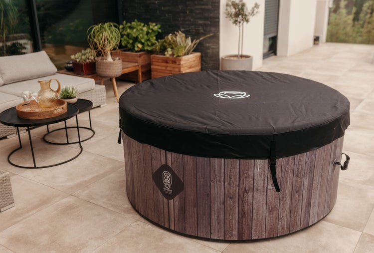 Runder Whirlpool in Holzoptik mit schwarzer Abdeckung auf einer modernen Terrasse mit Loungemöbeln und Pflanzen.