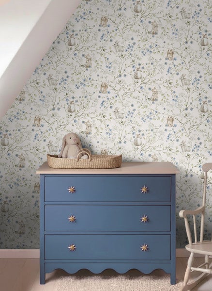 Kinderzimmer mit Tapete mit Hasen- und Blumenmuster, Kommode mit sternförmigen Griffen und Weidenkorb.